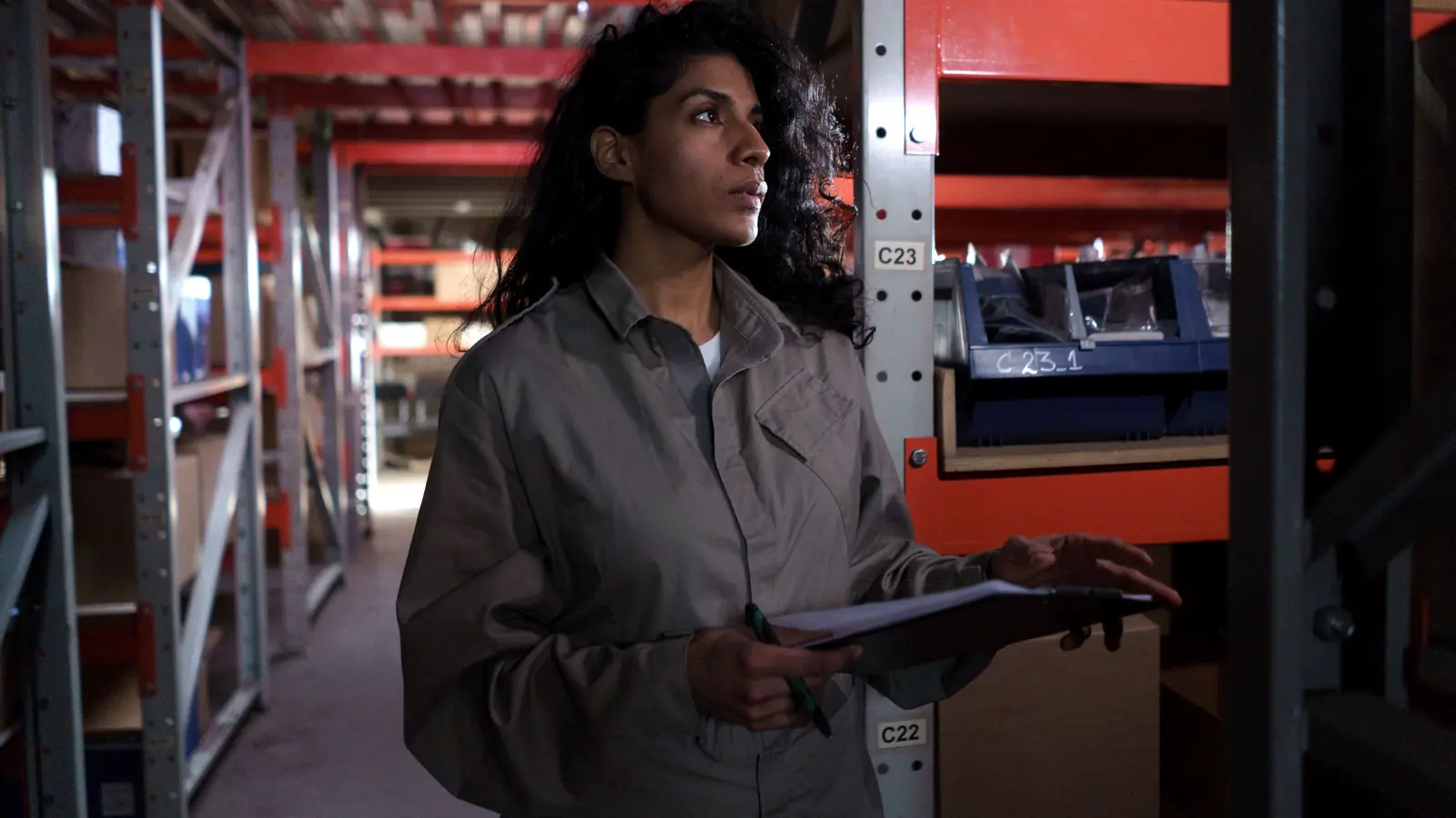 Warehouse worker holding a clipboard while checking labeled rack locations during an inventory audit.