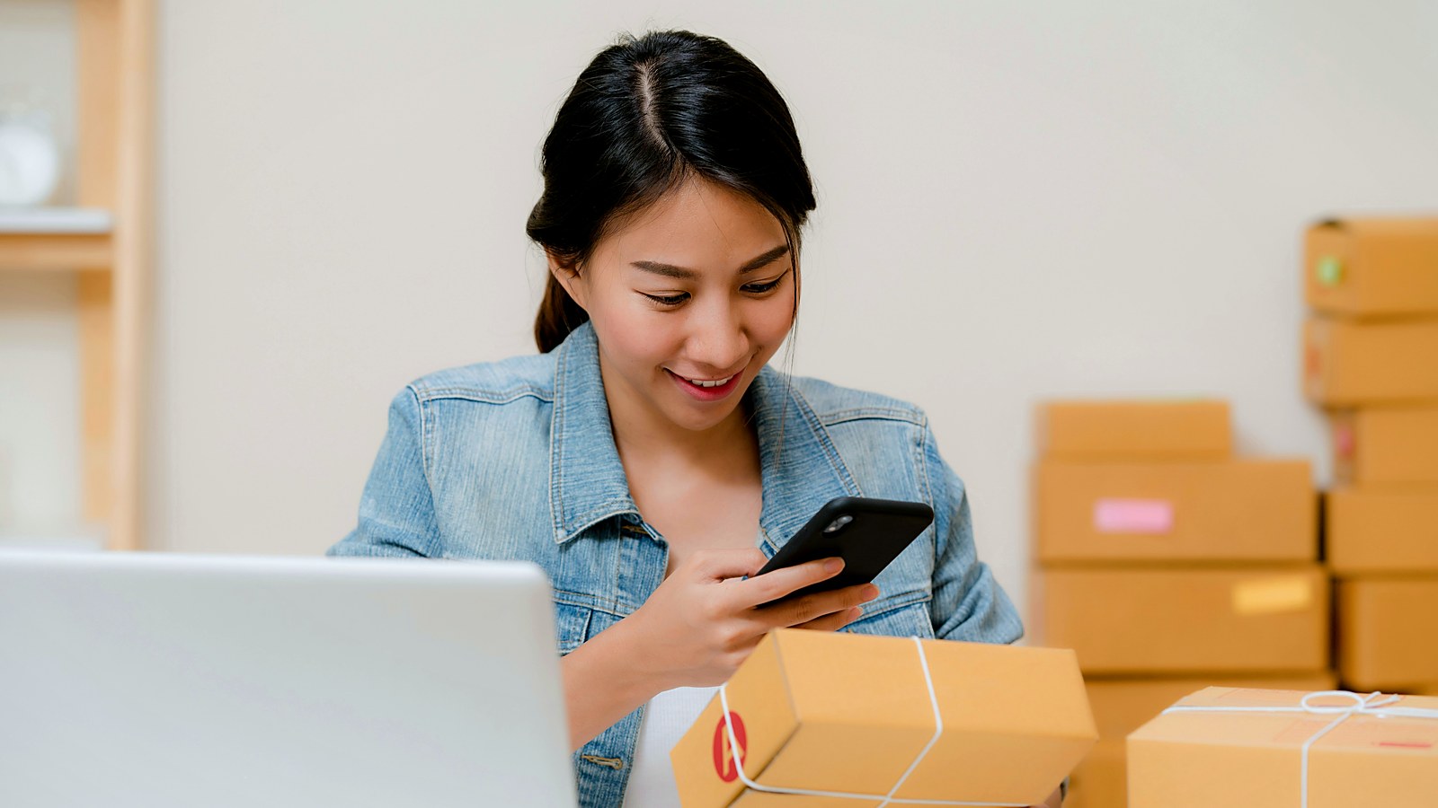 CPG founder checking her phone at a desk beside packed shipping boxes