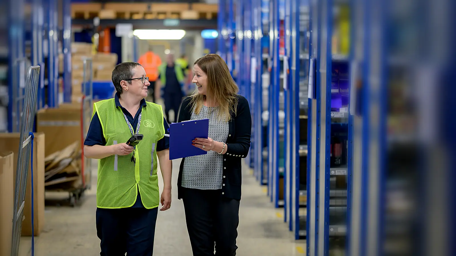 Warehouse team member and supervisor reviewing shipment paperwork on a clipboard in a distribution center aisle