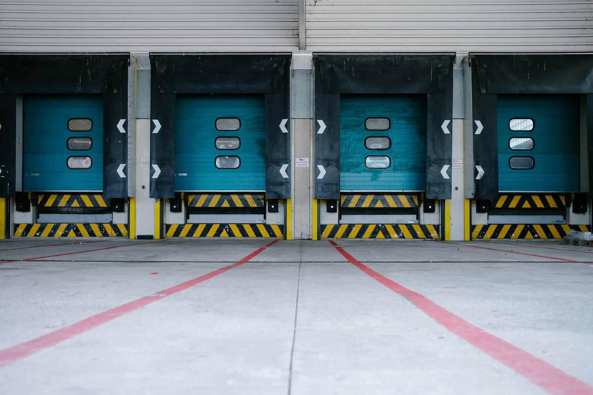 Row of four closed loading dock doors at an empty warehouse bay with no truck parked