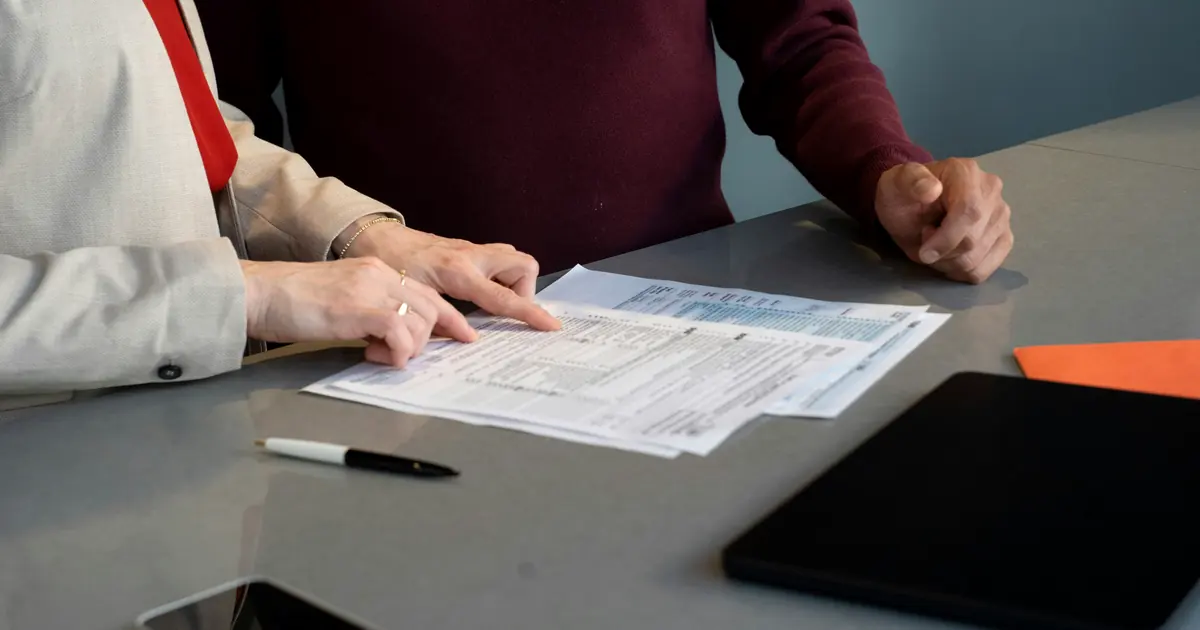 Two people comparing line items across overlapping printed reports at a desk.