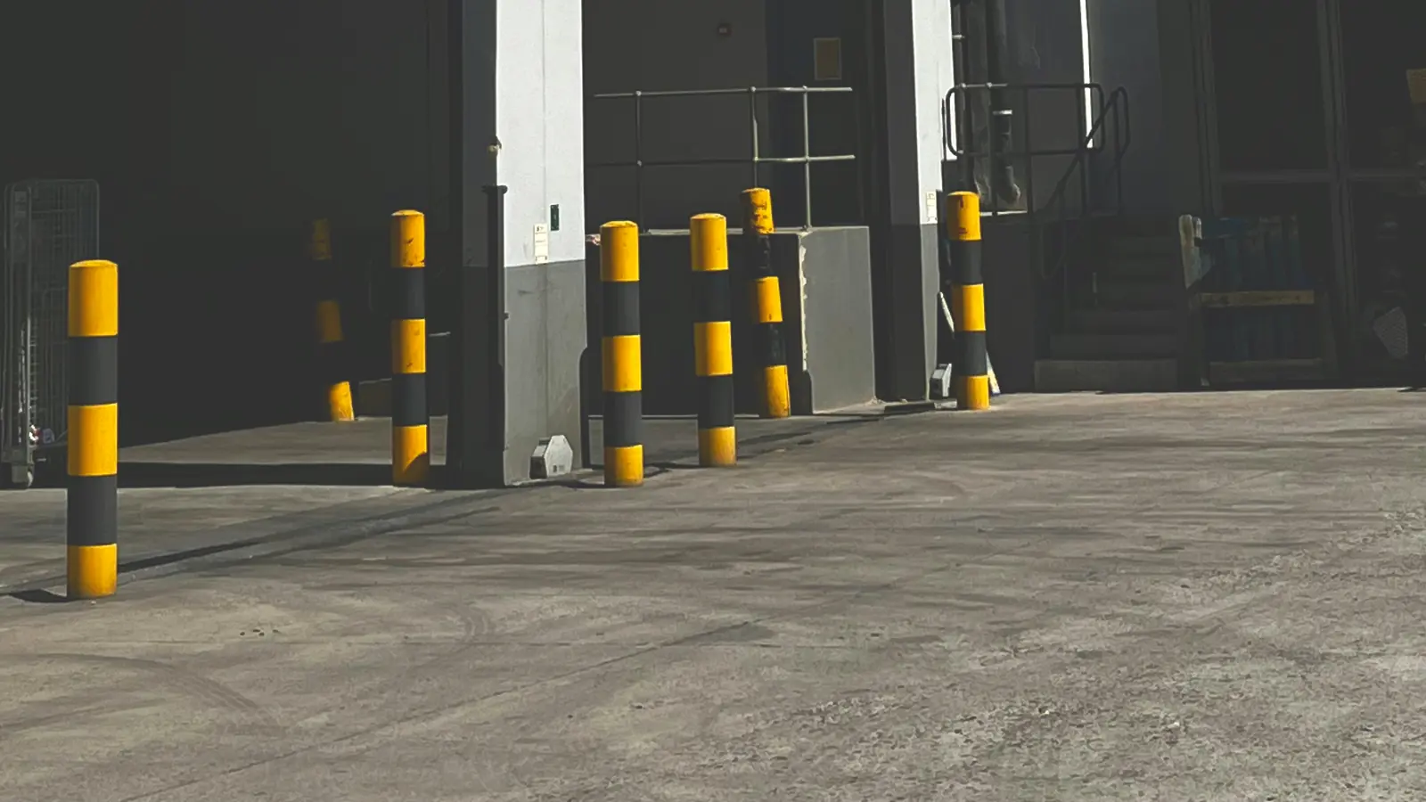 Empty receiving yard with safety bollards outside open warehouse dock doors, with no truck at the dock.