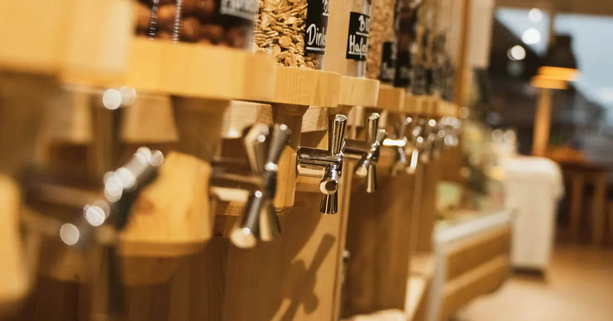 Wooden bulk dispensers of oats and grains with metal taps in a natural foods store.
