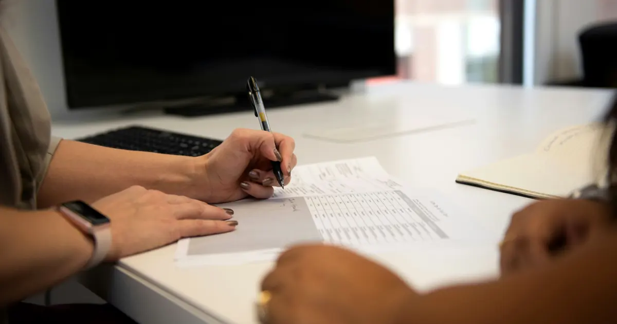 Two people at a desk reviewing a columnar rate sheet together, one holding a pen over the line items.
