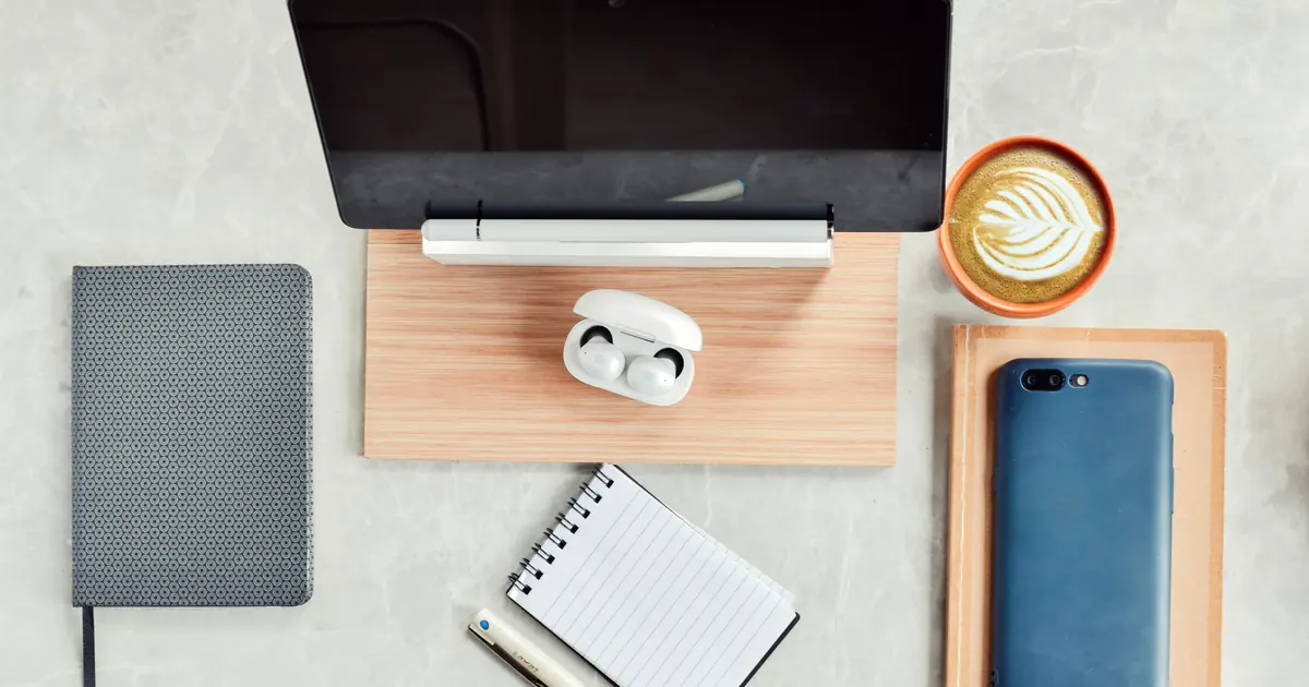 Overhead view of a tablet, notebooks, pen, phone, and a latte arranged on a desk.