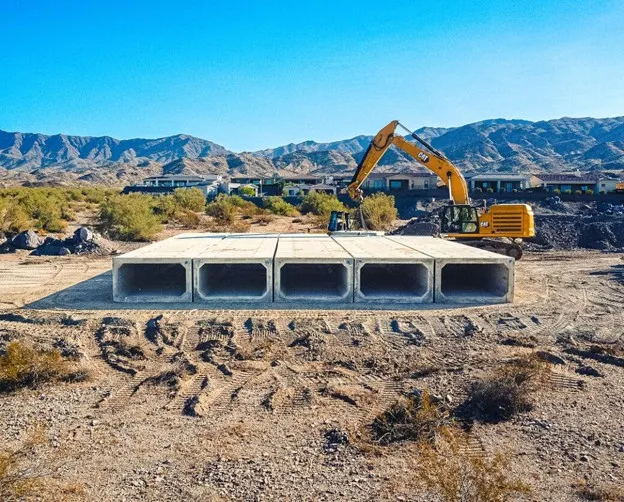 Precast box culvert sections laid out on a dry site with an excavator positioning them