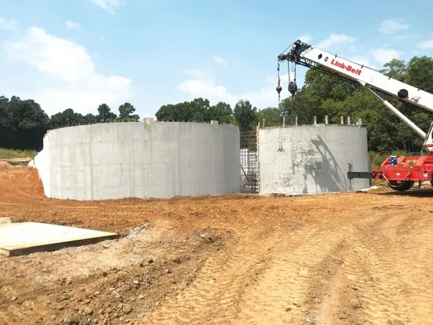 Two large circular concrete tanks under construction with a mobile crane alongside