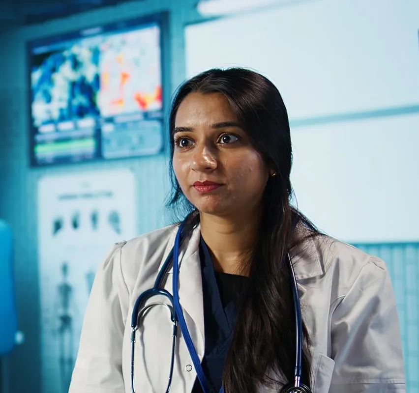 Female doctor with long hair wearing a white coat and stethoscope in a medical office.