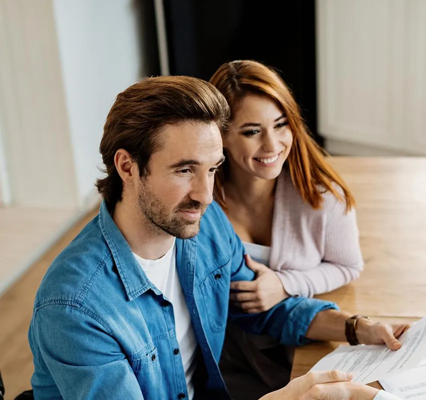 Smiling couple reviewing documents together at a table in a bright room.
