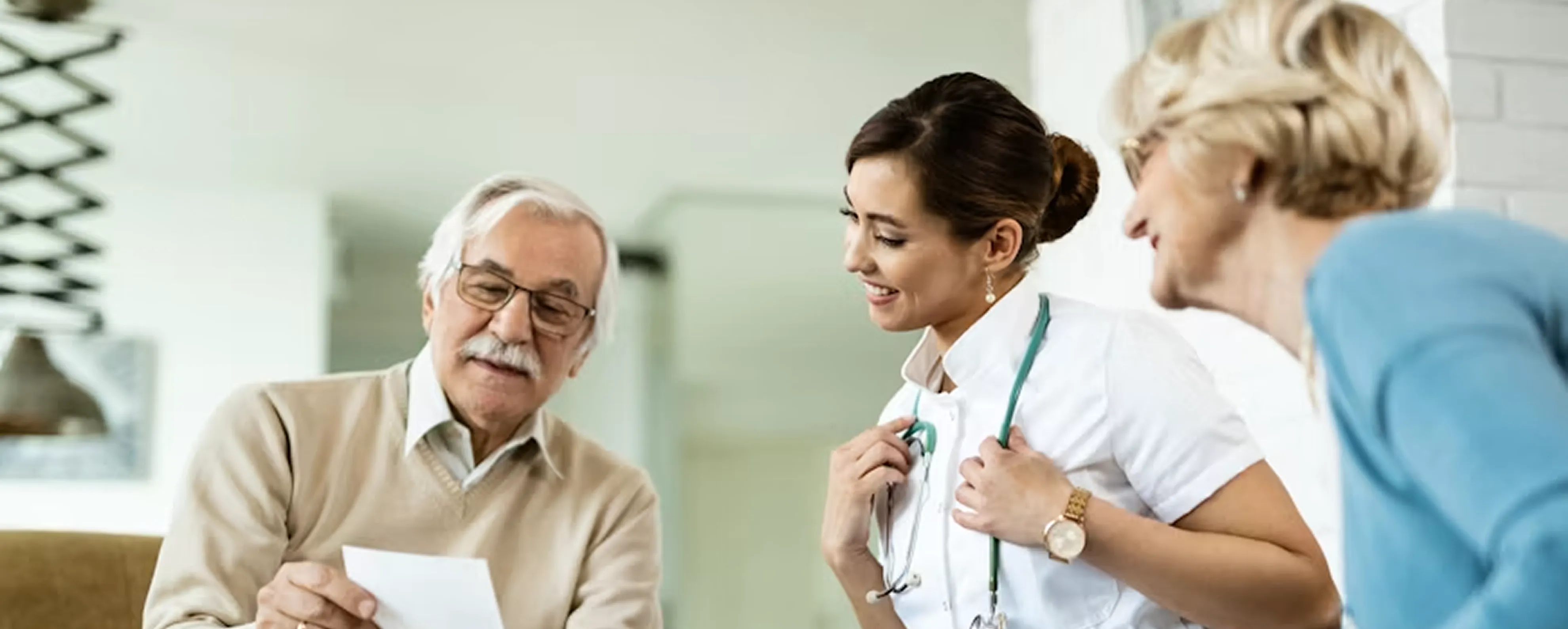 Young female doctor smiling and talking with elderly couple in a bright home setting.