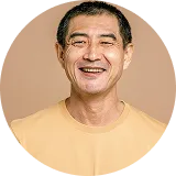 Smiling middle-aged Asian man wearing a light yellow shirt on a beige background.