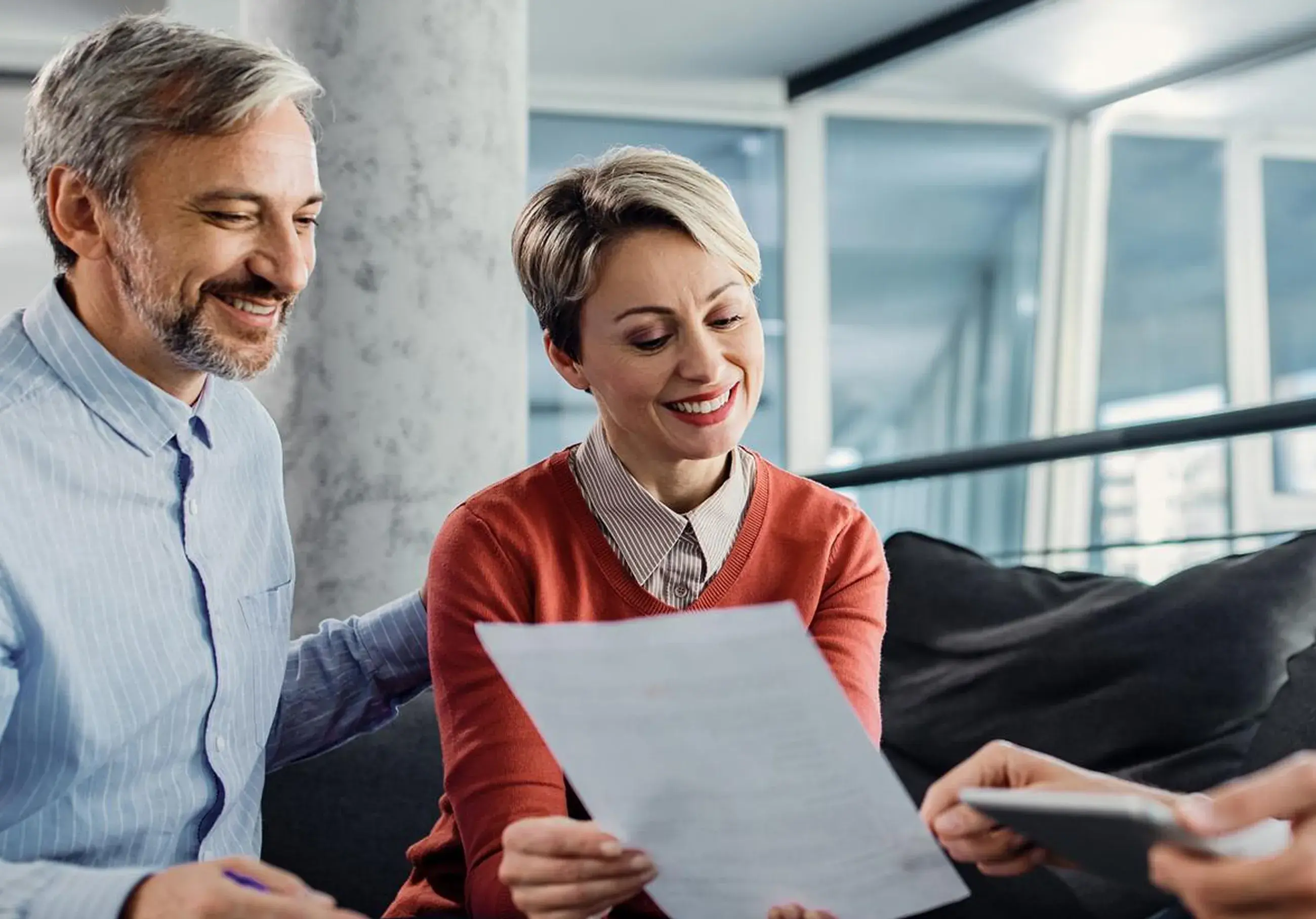 Smiling man and woman reviewing a document with a person holding a calculator nearby.