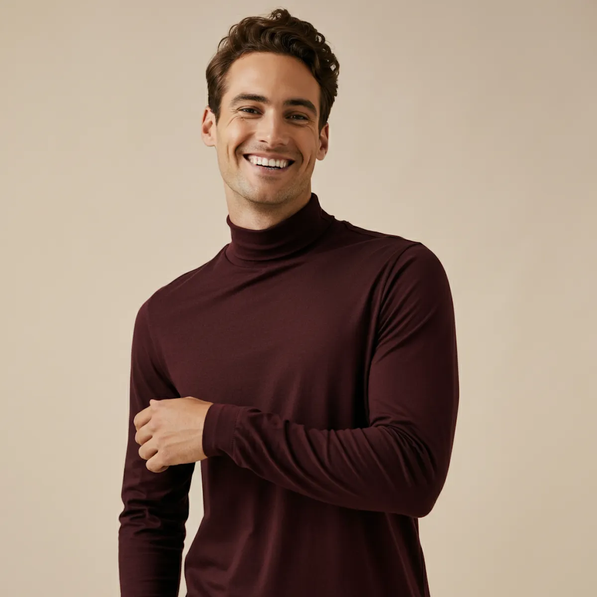 Smiling man with curly brown hair wearing a maroon turtleneck sweater against a beige background.