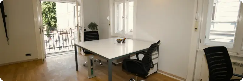 Bright office room with a white table, three black chairs, open balcony door, and windows.
