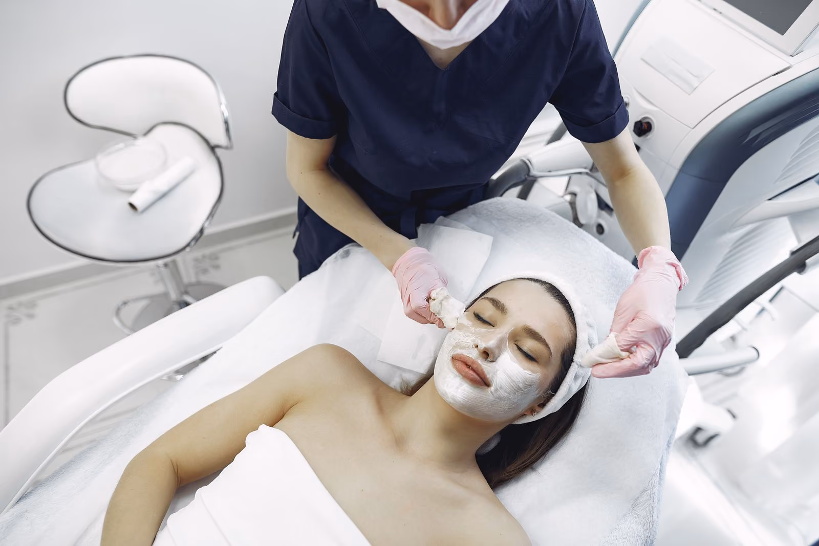 Woman with eyes closed getting a facial treatment with cream in a spa by a beautician.