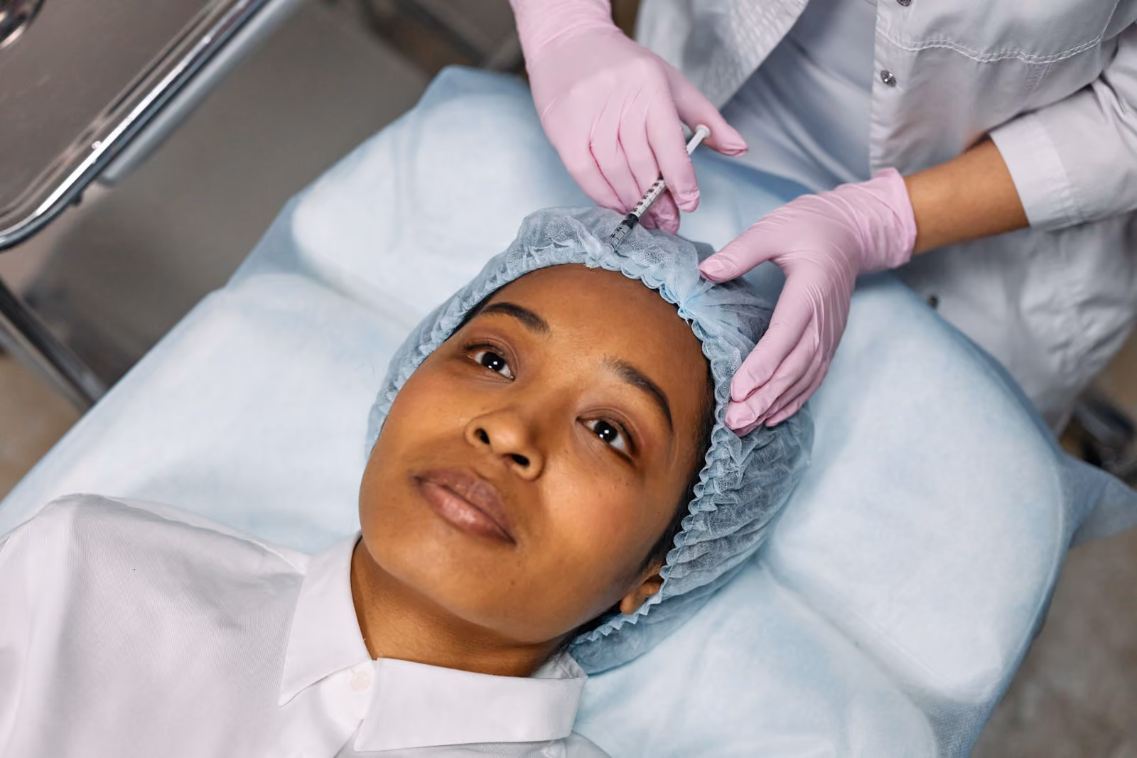 Medical professional in pink gloves injecting a patient's forehead while she lies on a treatment bed.