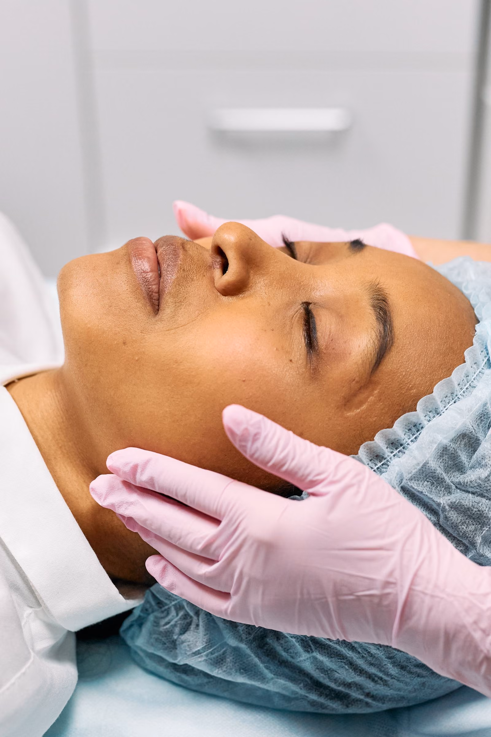 Woman receiving facial treatment with hands in pink gloves gently touching her face.