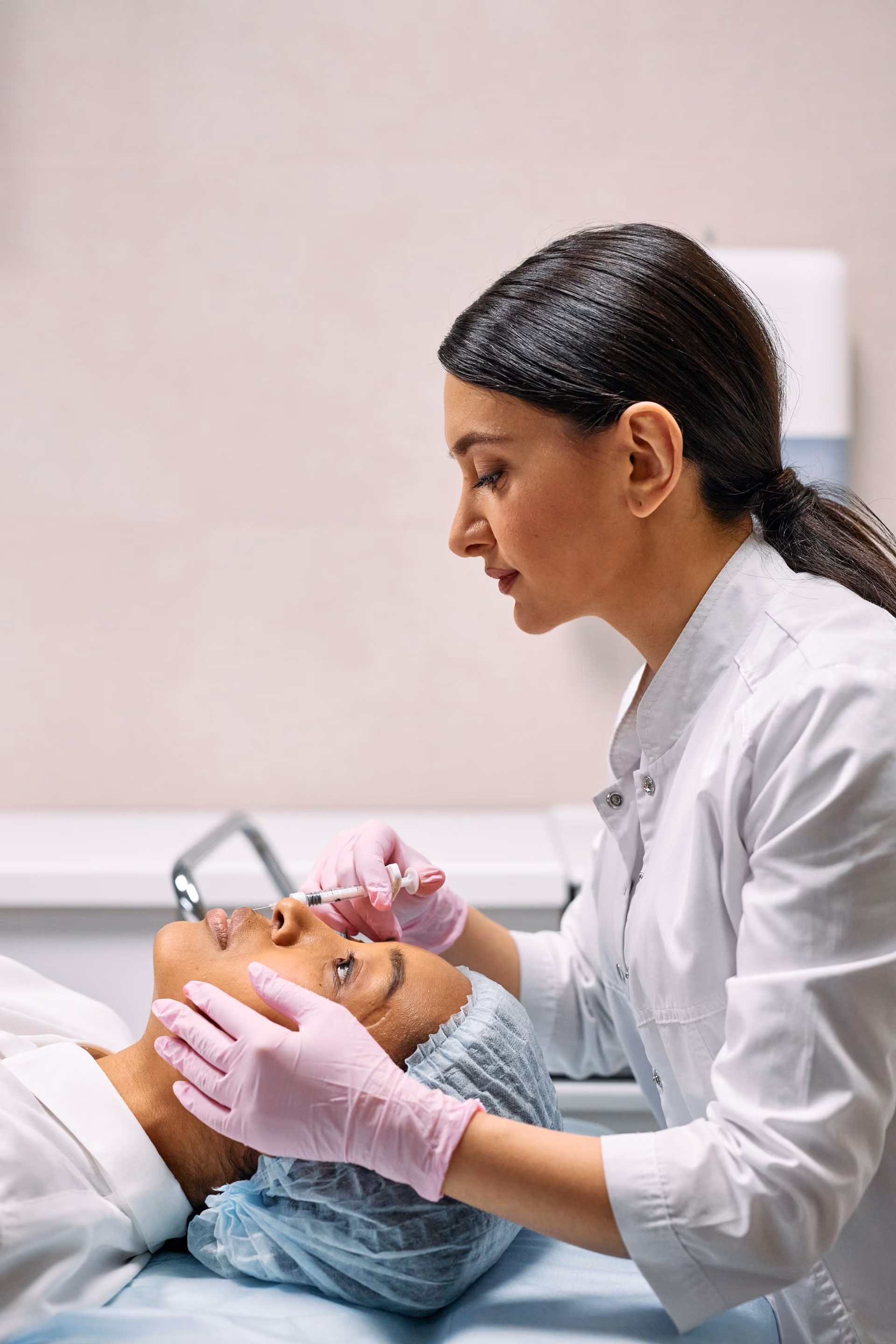 Doctor in pink gloves administering injection to patient's nose in a clinical setting.