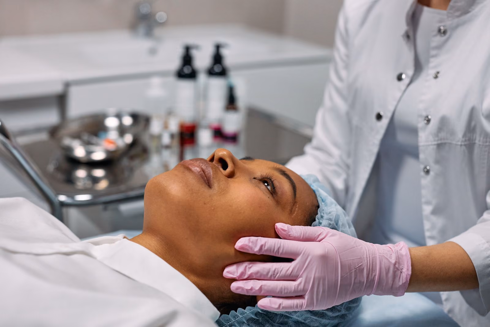 Close-up of woman receiving facial treatment from a person wearing pink gloves in a clinic.