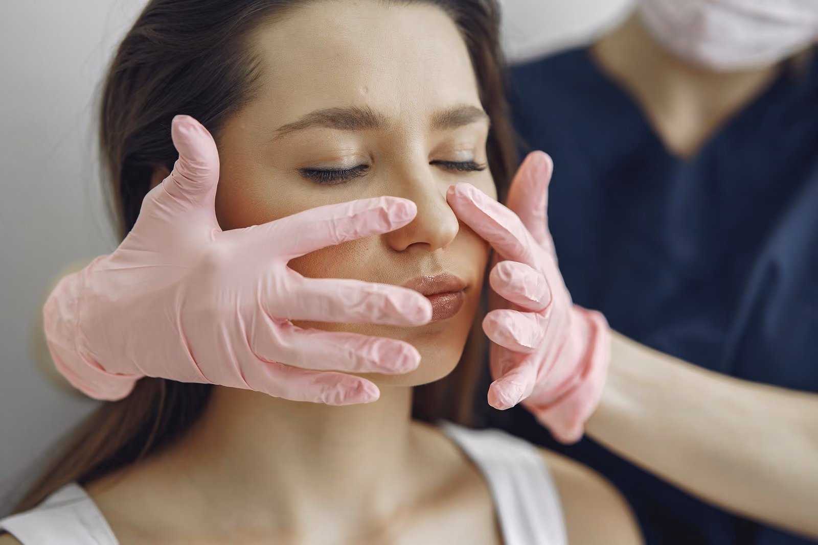 Person with closed eyes receiving facial skin examination by a gloved professional.