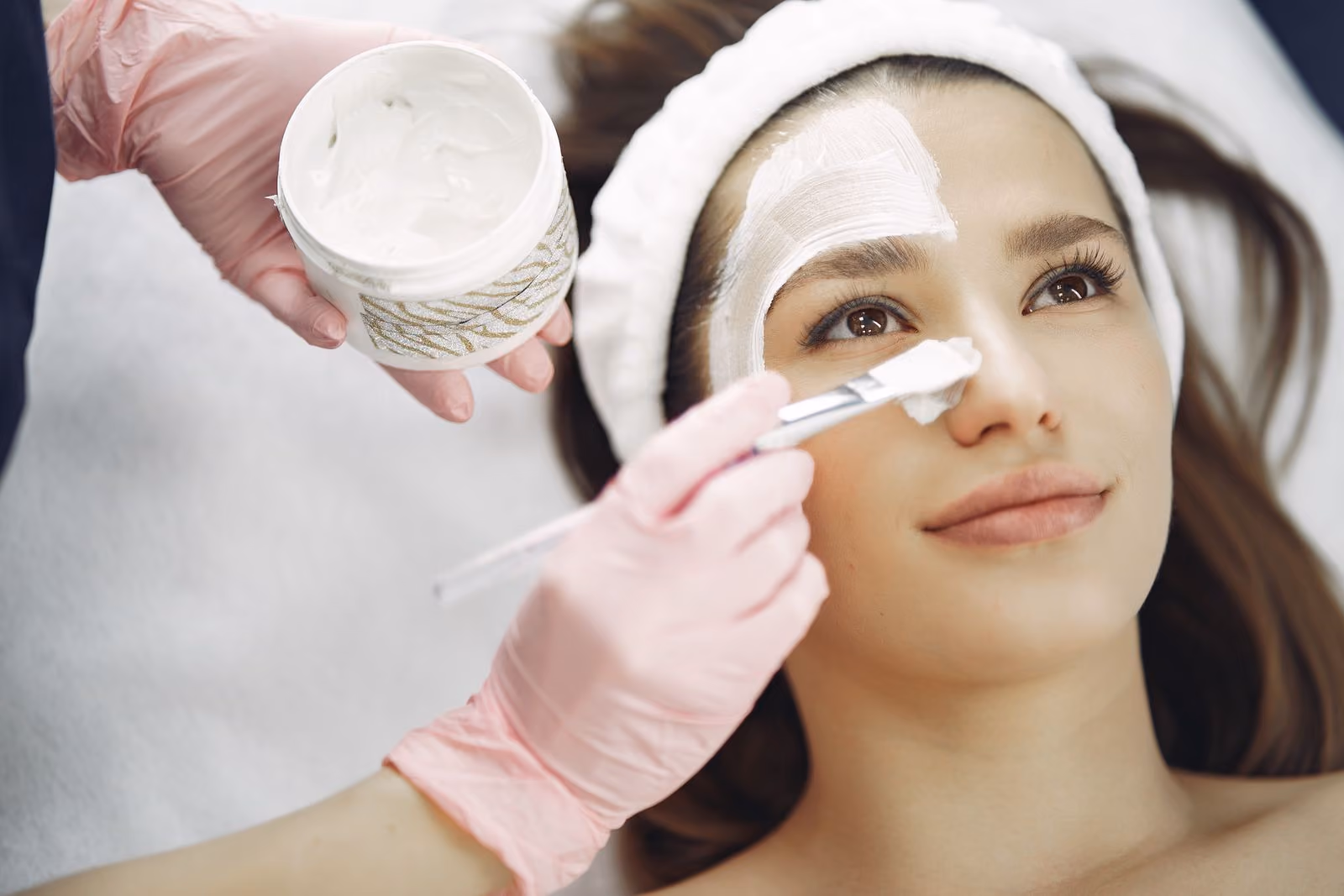 Woman receiving a facial treatment, cream being applied to her face with a brush.