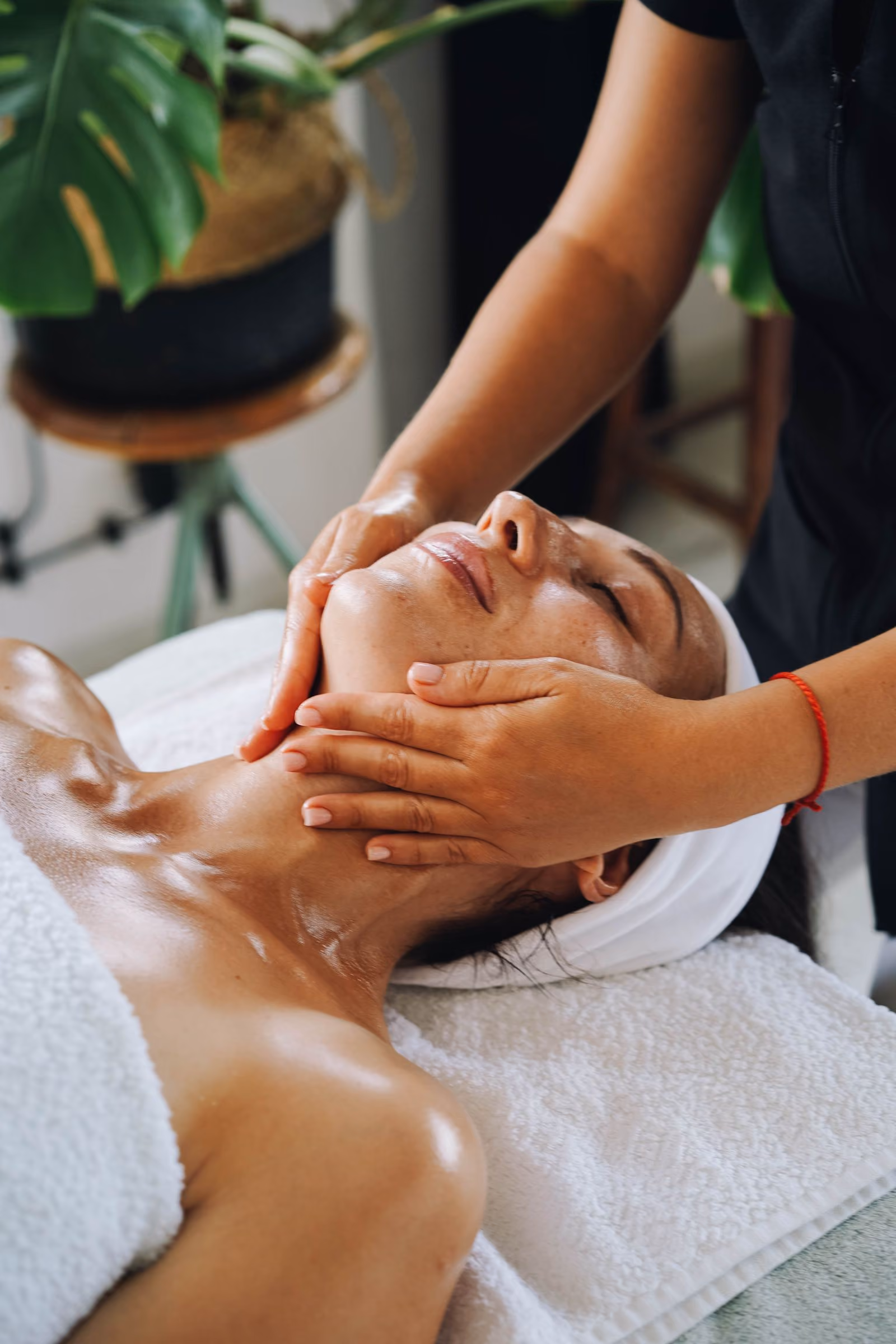 Woman receiving a relaxing facial massage at a spa with a white towel headband.