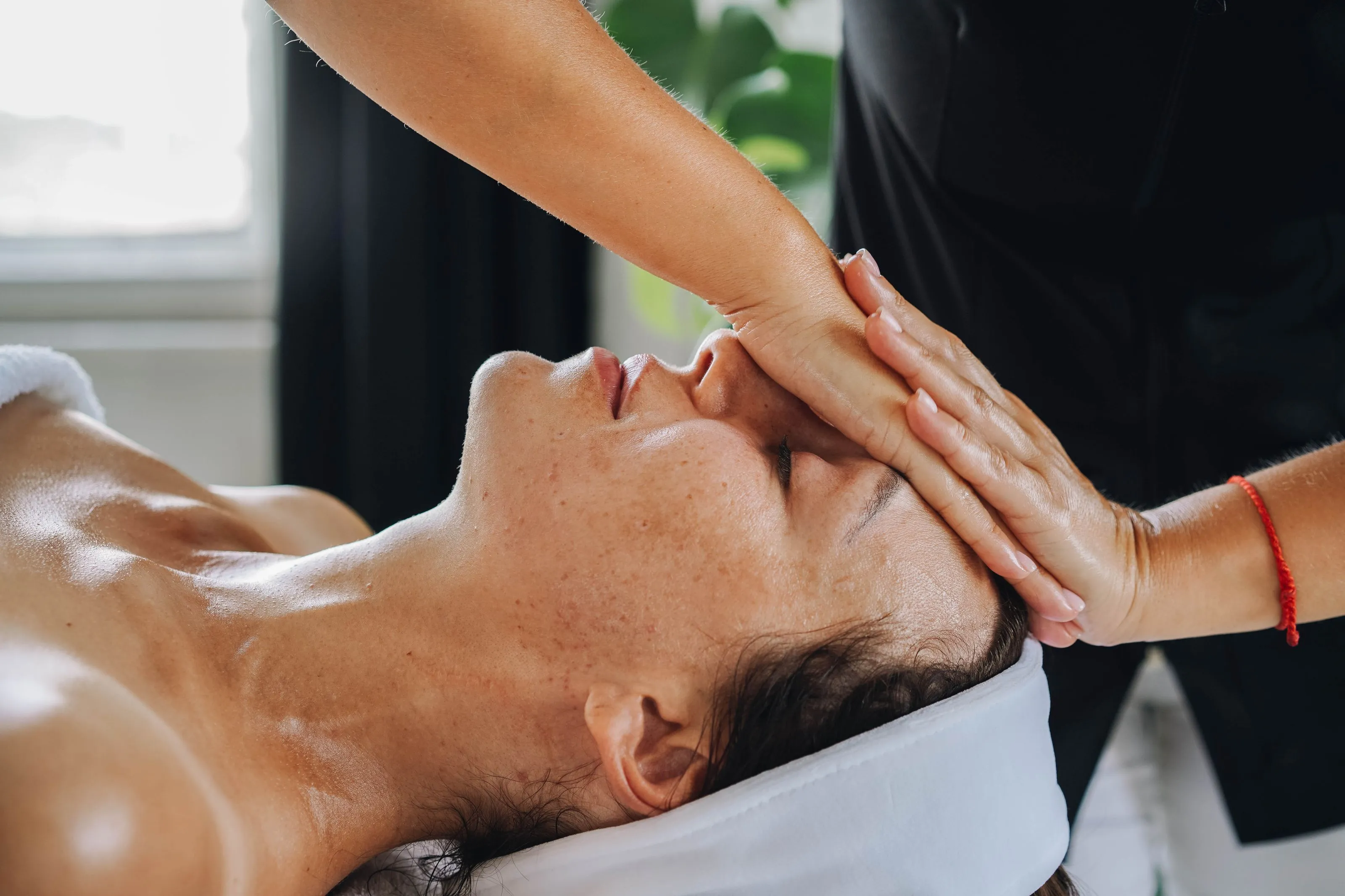 Woman receiving a forehead massage while lying down with eyes closed and a white headband.