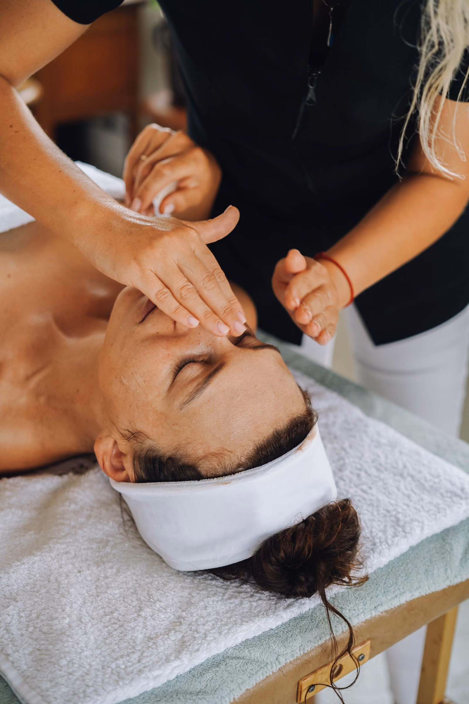 Woman receiving a facial massage while lying on a spa bed with a white headband.