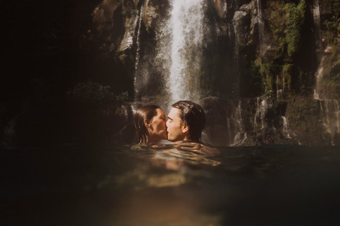 Séance photo intimiste d'un couple s'embrassant à fleur d'eau dans le bassin d'une cascade majestueuse au cœur de la Réunion.