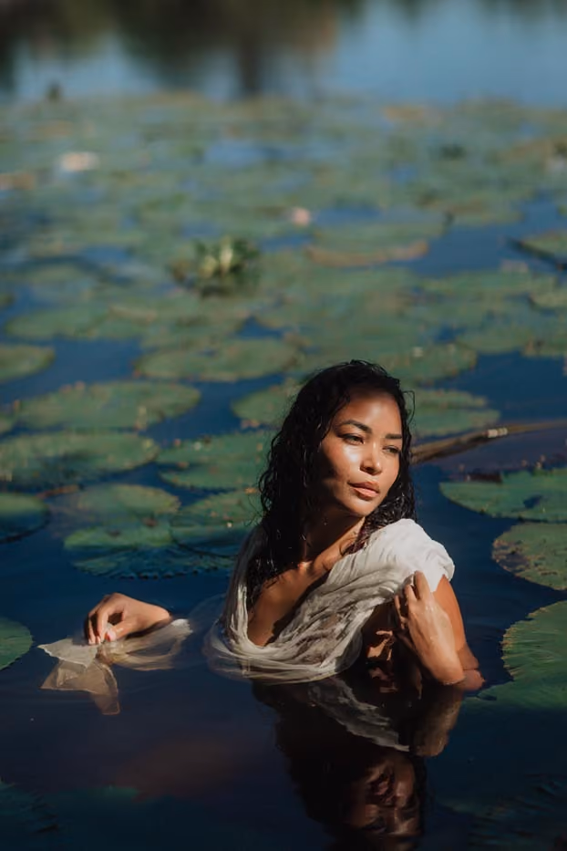 Plan large d'une séance photo portrait en extérieur d'une femme posant dans un bassin de nénuphars à la lumière du soleil couchant à l'Étang Saint-Paul.