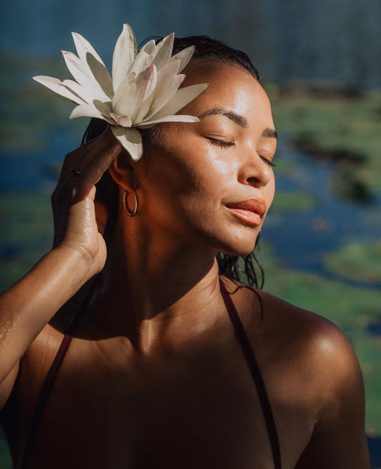 Plan serré du visage d'une femme posant dans un bassin de nénuphars à la lumière du soleil couchant à l'Étang Saint-Paul. Sa main proche de son visage tient une belle fleur de nénuphare.