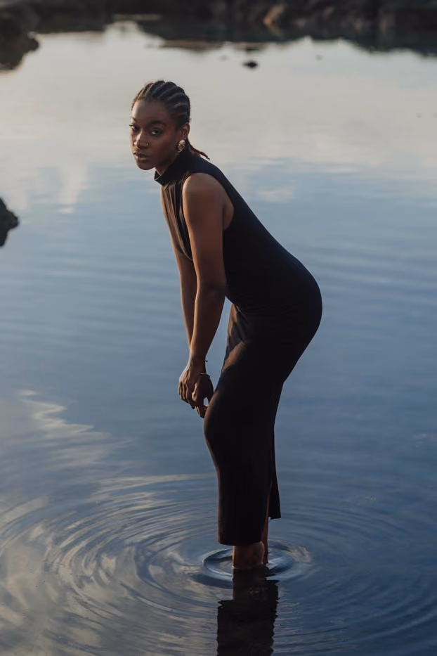 Séance photo portrait de Youmna en robe longue noire, debout les pieds dans l'eau d'un bassin naturel à la Réunion.