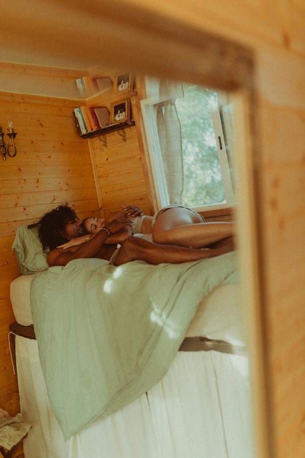 Reflet dans un miroir d'un couple enlacé de manière intimiste sur le lit d'une tiny house en bois au Portugal