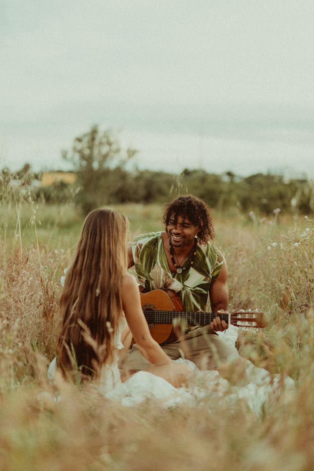 Séance photo de couple intimiste en extérieur au Portugal, un homme jouant de la guitare dans un champ face à sa compagne.