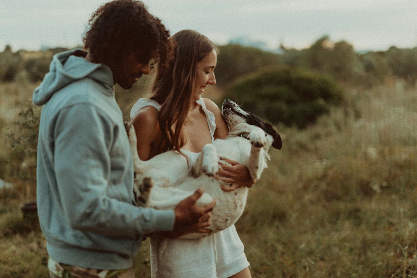Un couple sourit chaleureusement en portant ensemble leur chien noir et blanc au milieu de la nature.