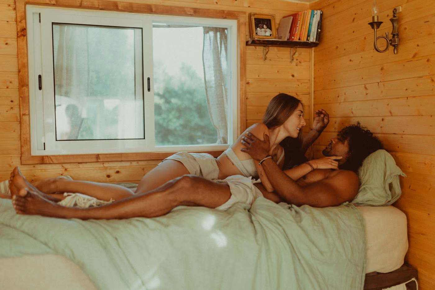 Séance photo de couple à l'intérieur d'une tiny house lumineuse, un homme et une femme allongés complices sur un lit.