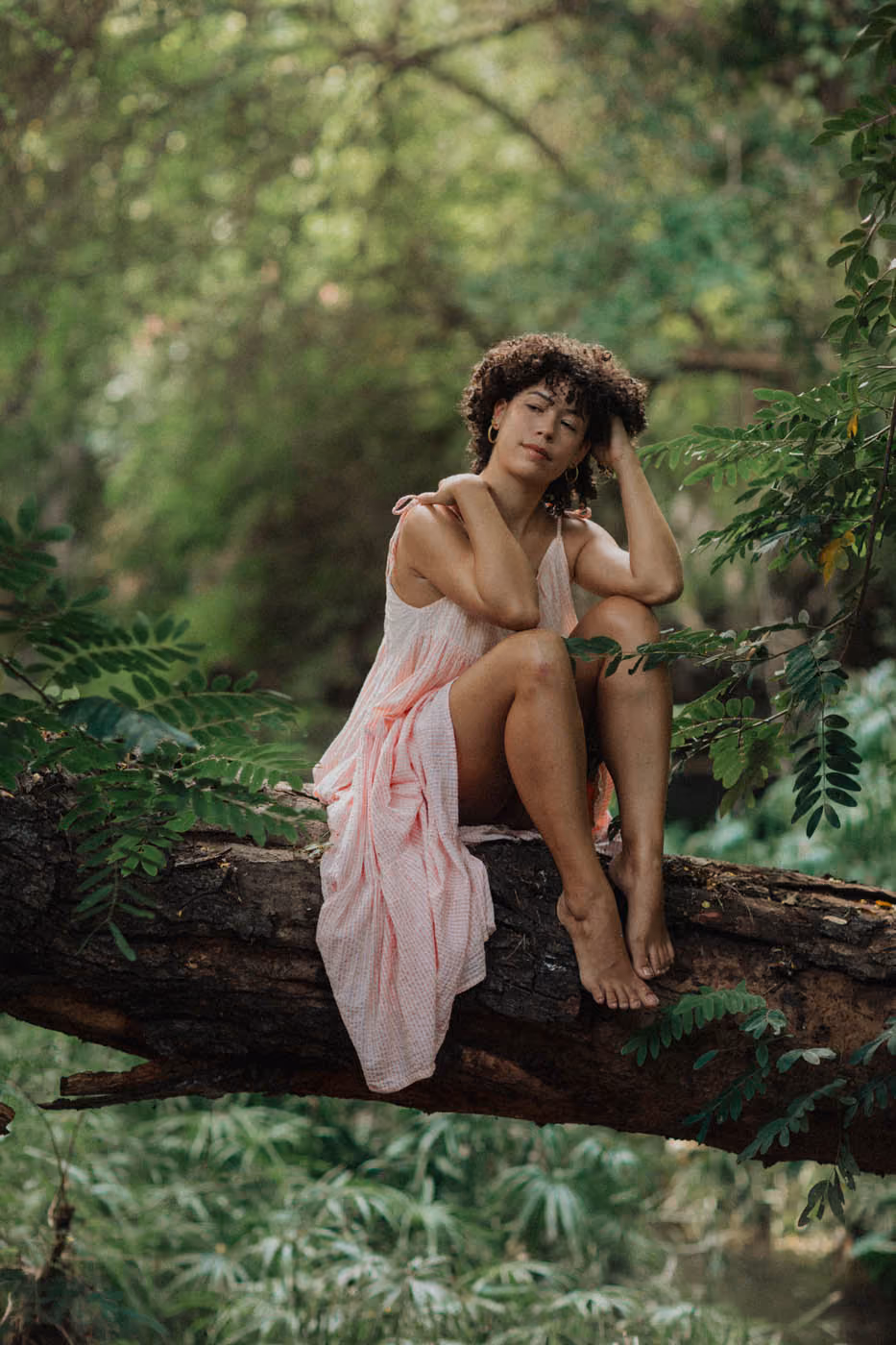 Portrait intimiste de l'artiste peintre Pauline, pensive et assise pieds nus sur une branche d'arbre au cœur d'une nature sauvage.