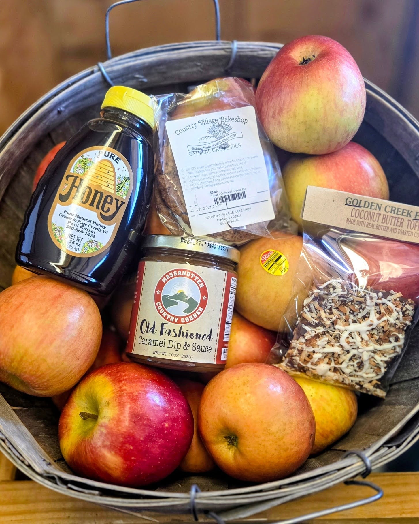 Basket with apples, honey bottle, caramel dip, oatmeal creme pie, and coconut butter toffee treat.