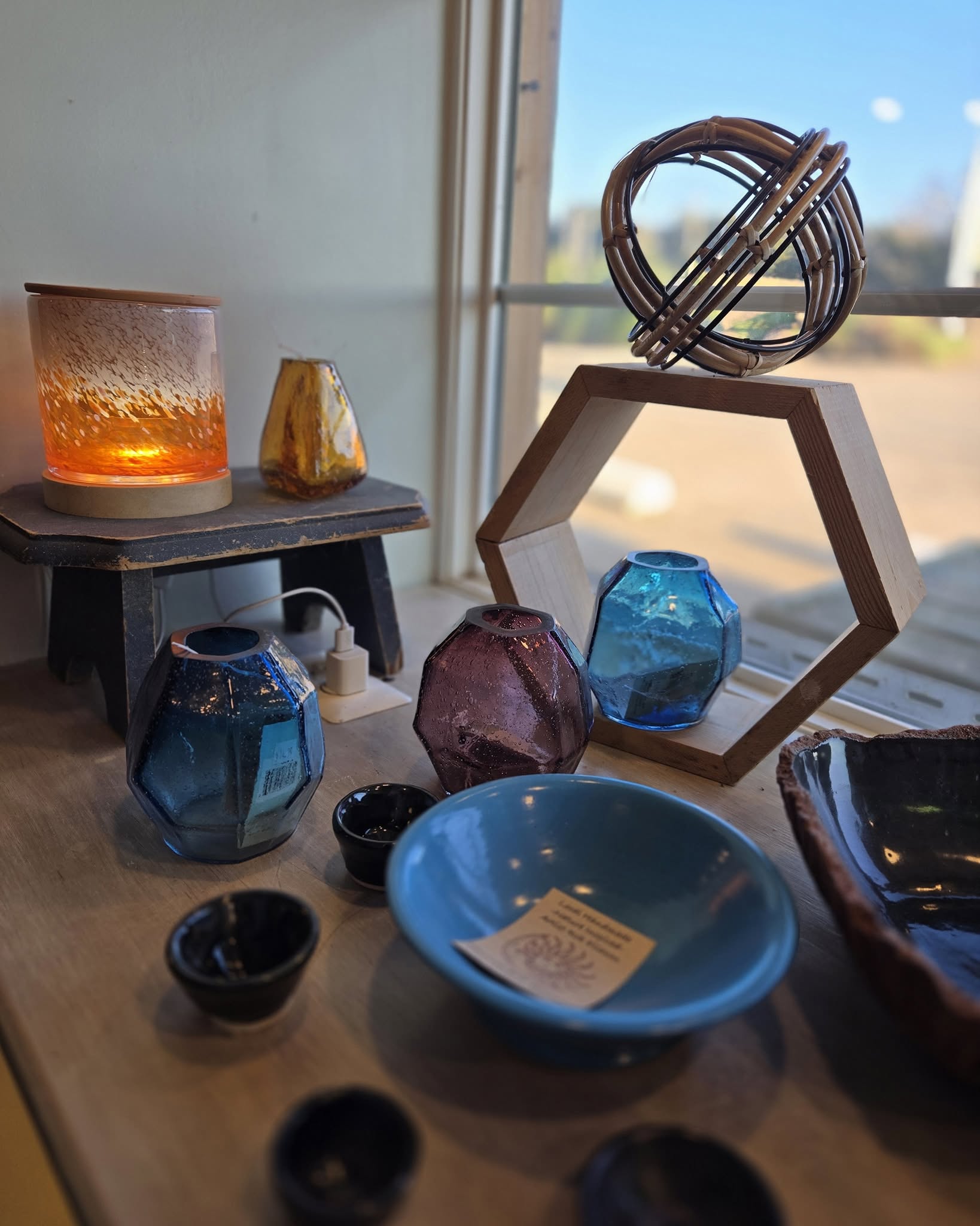 Assorted decorative glass and ceramic objects arranged on a wooden table near a window.