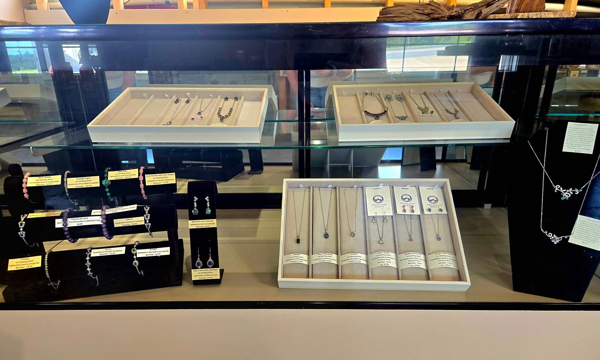 Display case with various gemstone and silver jewelry including bracelets, necklaces, and earrings with price tags.