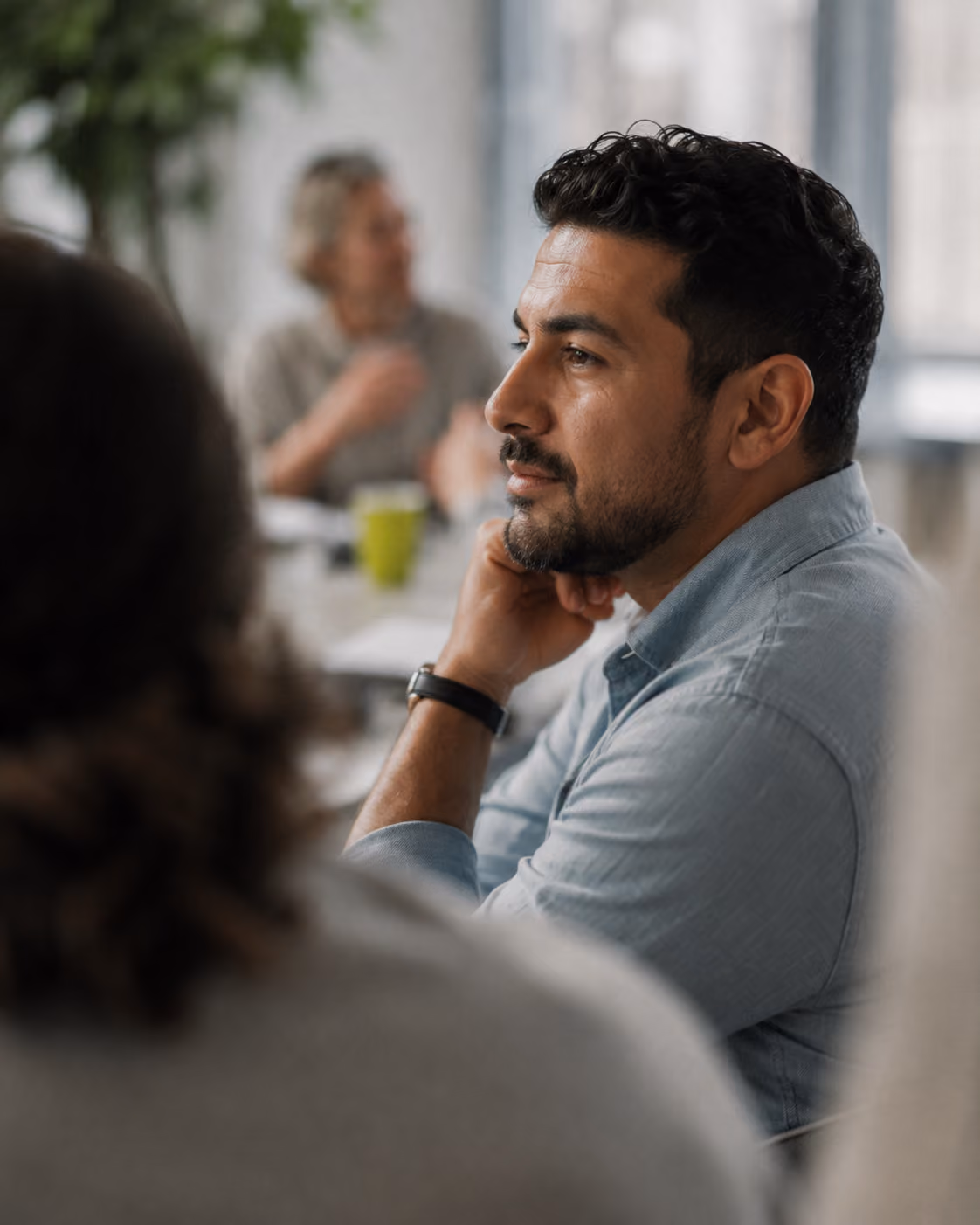 Man with beard resting chin on hand attentively listening in a meeting room.