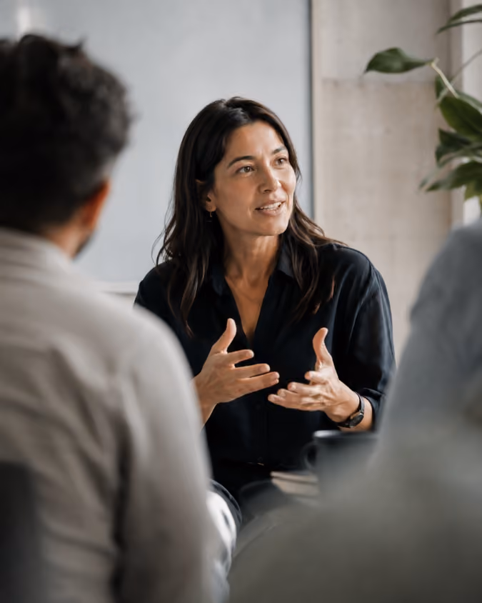 Woman in black shirt speaking and gesturing with hands during a meeting with two others.