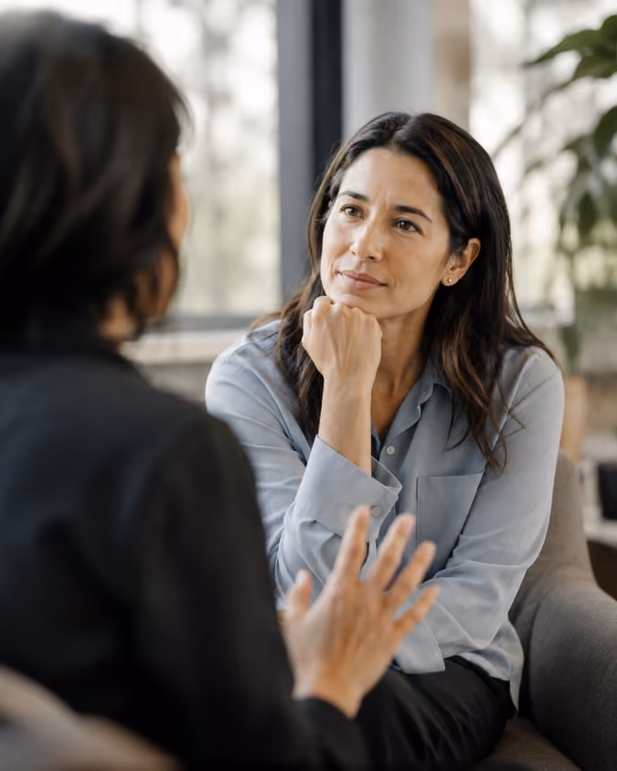 Woman attentively listening to another woman speaking in a modern office setting.