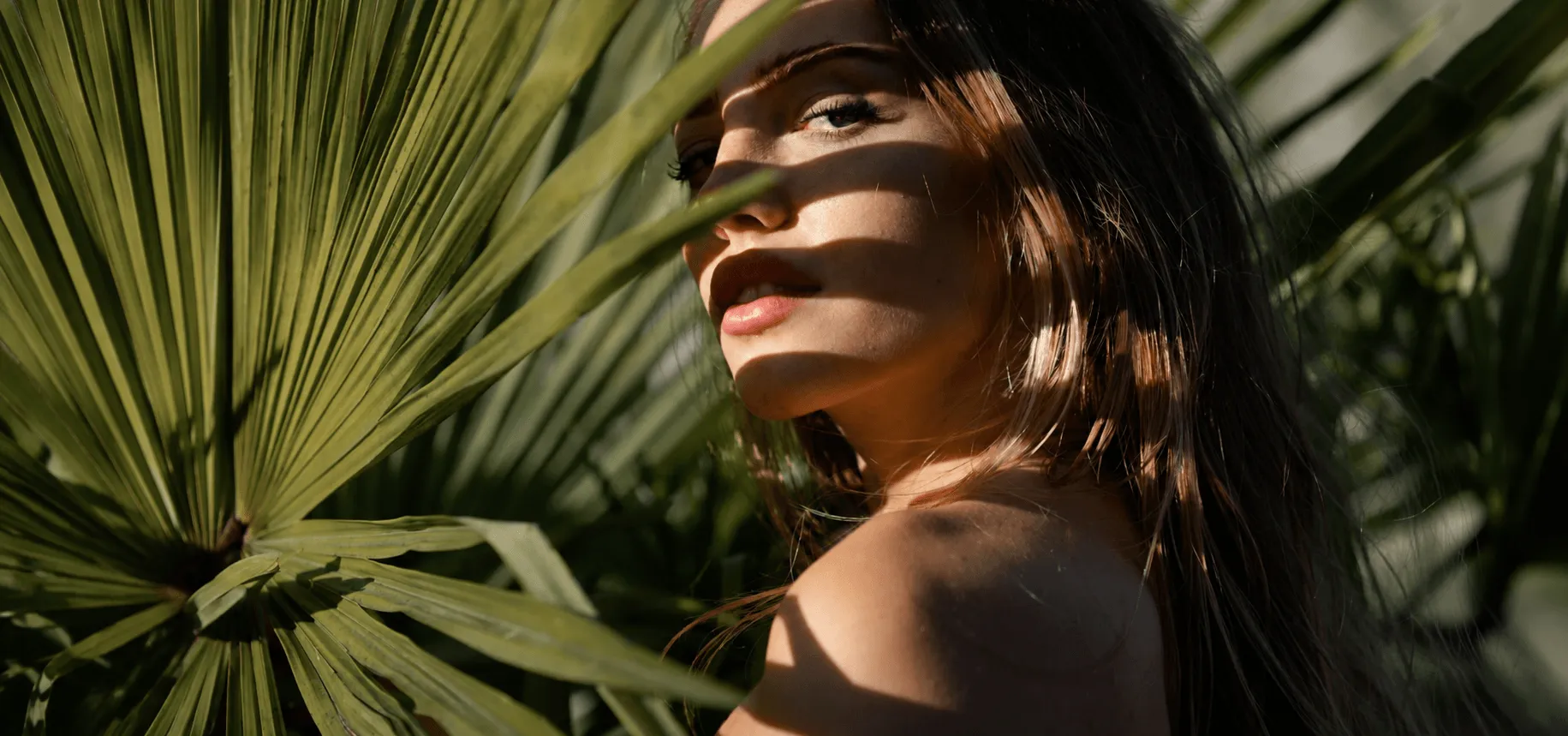 Woman with glowing skin among palm leaves