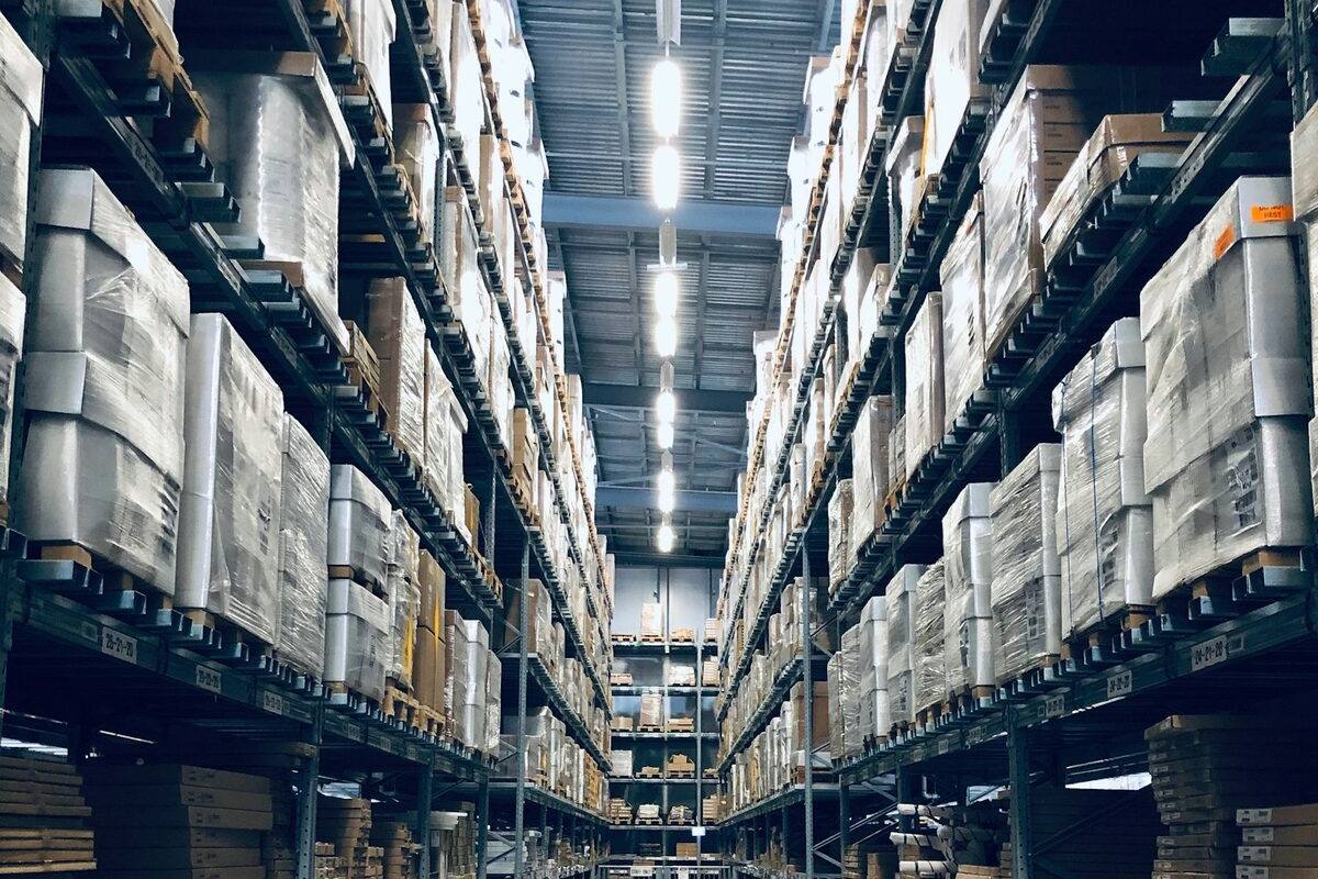 A high warehouse aisle with pallet racking on both sides and a row of lights on under the ceiling