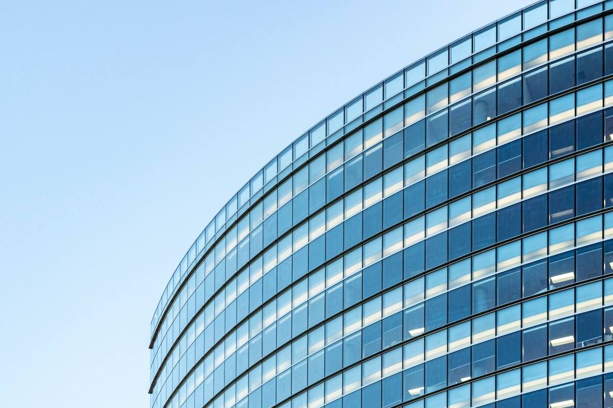Glass facade of a modern office building with interior lighting visible on some of the floors