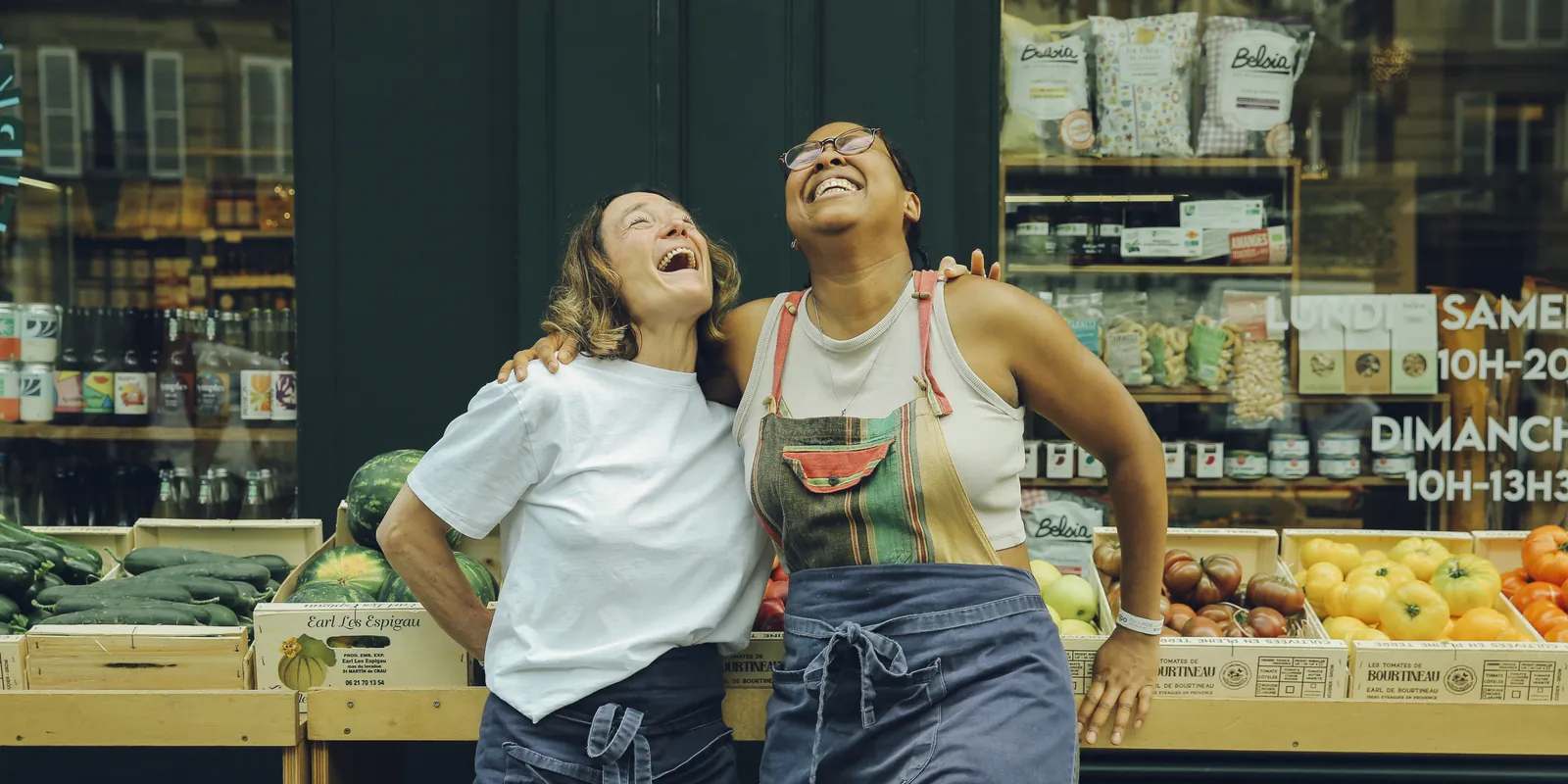 Deux vendeuses Champs Libres riant devant l'étal de fruits et légumes de l'épicerie, Paris