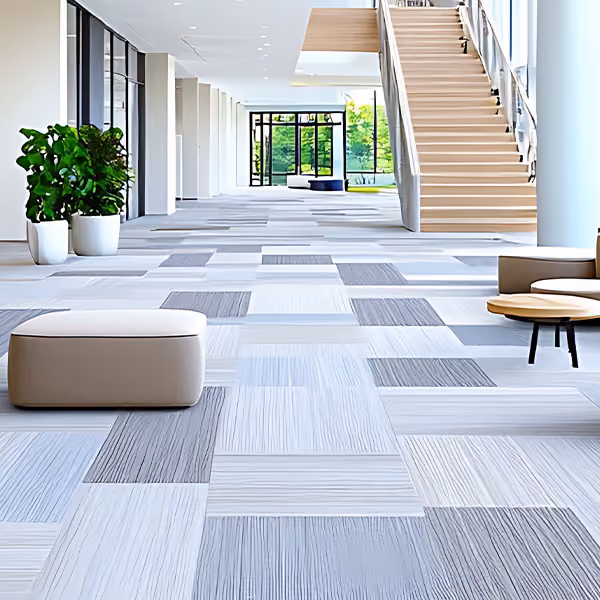 University common area with patterned gray and beige flooring, plants, seating, and staircase.