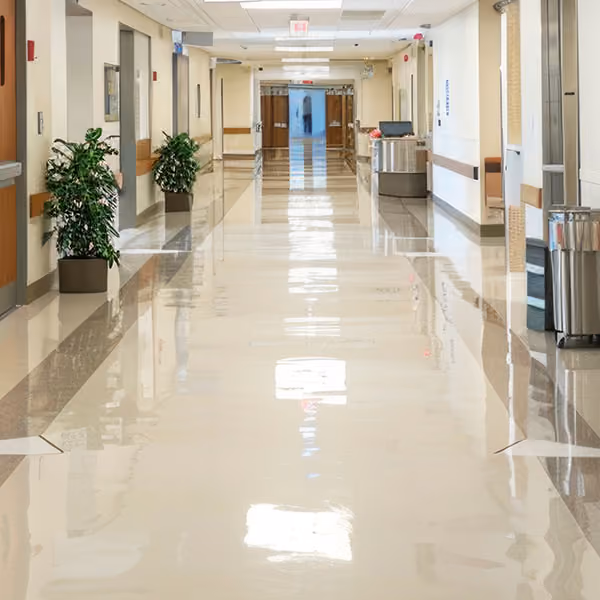 Shiny, clean hospital hallway with plants, elevator doors, and a reception desk in the distance.