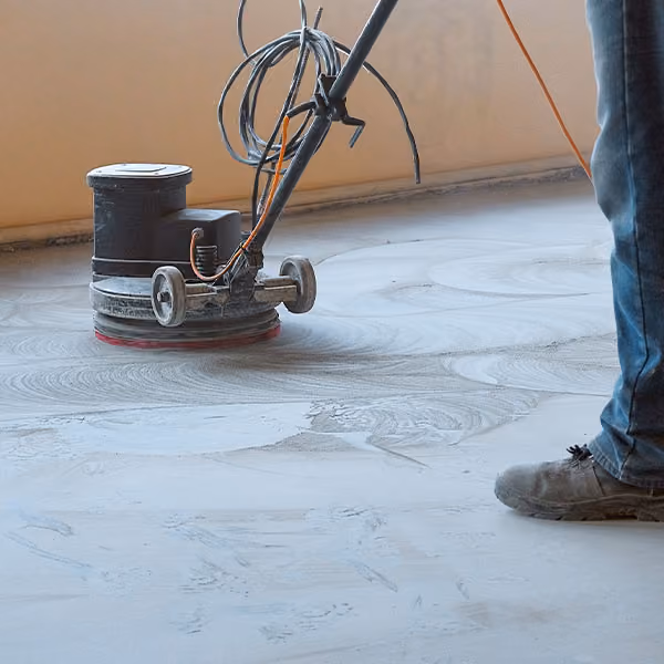 Worker operating a floor grinder machine to prep a concrete floor surface indoors.